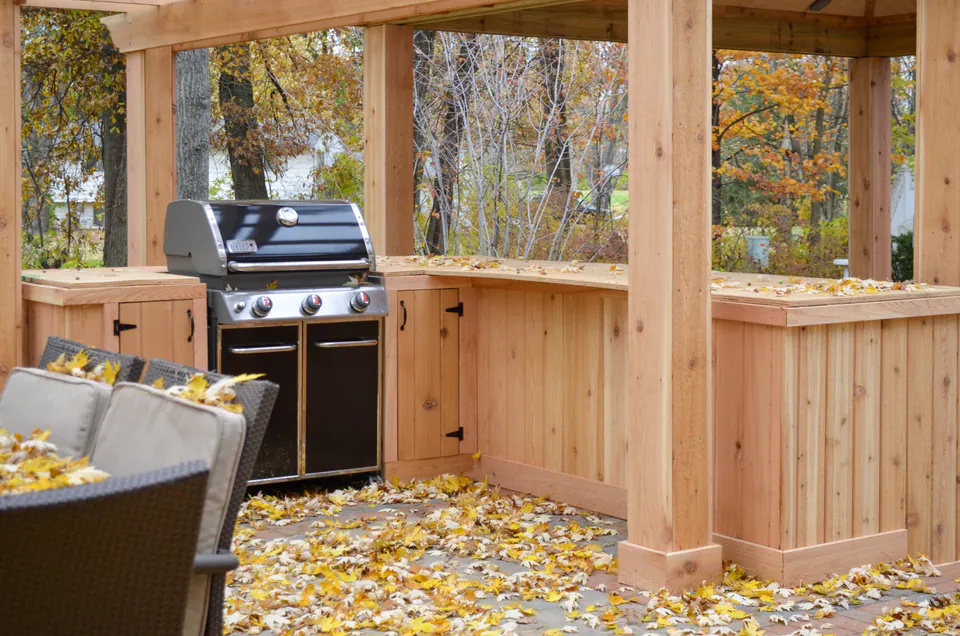 Close view of built-in grill and wood counter under pavilion framing with paver patio and fall leaves.